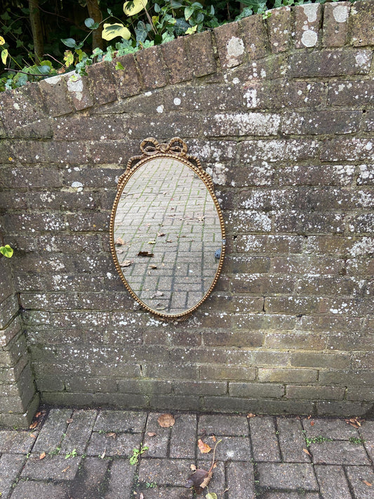 ornate metal framed oval mirror. gilt metal frame. ribbon detail. vintage mirror