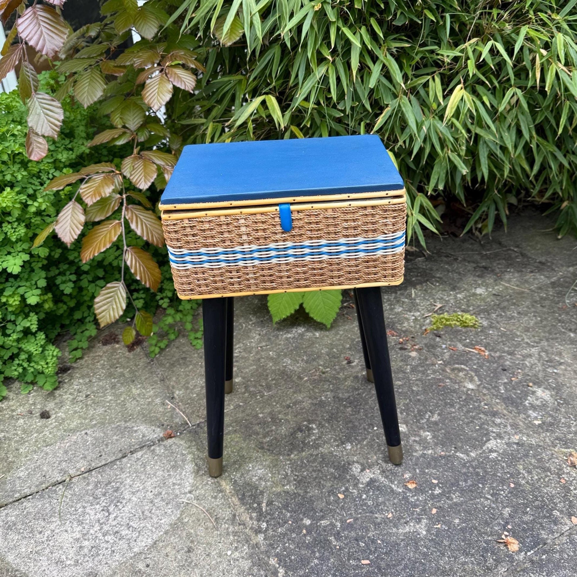 1950s small work box or sewing basket on lovely tapered retro mid century legs. Wicker basket with painted blue lid. Lovely blue detail. Black painted legs with metal capped feet. craft box, retro style.