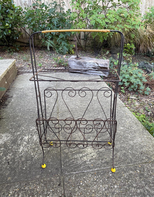 a mid century scrollwork black metal work storage rack. with a plastic yellow wrap around handle and yellow round feet. Very retro and mid century. Rusted finish currently