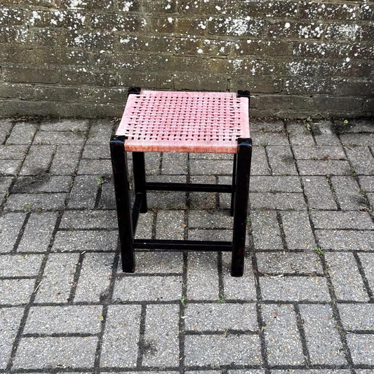 black framed painted wooden stool with a pink woven seat. retro in style. needs some tlc. good condition